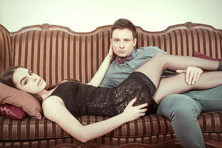 Retro vintage couple lying on the retro furniture. Young man and woman In sexy edition looking seductively at camera or at you. Vintage male and female model on sofa at home.の写真素材
