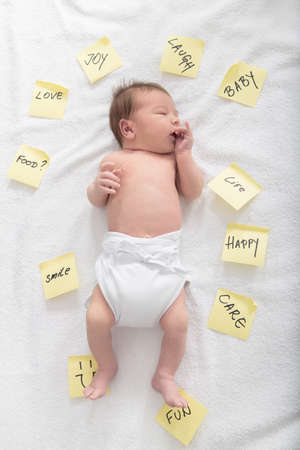 Cute baby surrounded by post it stickers with beautiful words , Notepapers on bed around carefree baby , Idyllic photo of child with sticky notes all around with words love happy care fun smile laughの写真素材