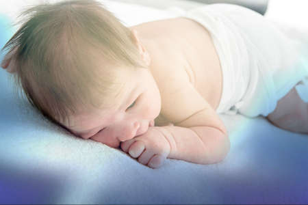 Beautiful newborn baby resting on warm blue blanket sucking thumb , Cute little baby lying down on soft blanket in bedroom wearing diapers , Happy and healthy childhood concept on dreamy blue ambientの写真素材