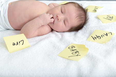 Innocent baby with thoughts written on sticky notes all around , Adorable baby lying on soft white blanket surrounded by post it stickers showing meaning of life with words love joy smile laugh happyの写真素材
