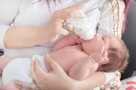 Cute serene baby drinking milk out of bottle in mother's lap , Image of adorable baby drinking milk...
