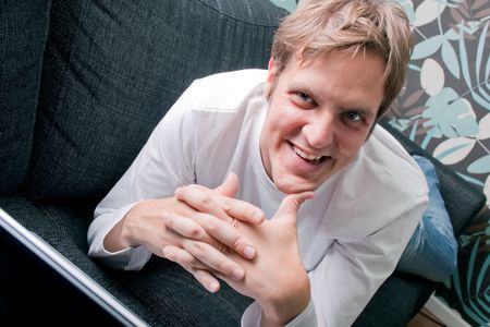 Young man lying on couch and working on laptopの写真素材