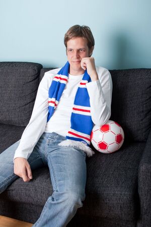 smiling young man supporting his football team on tvの写真素材