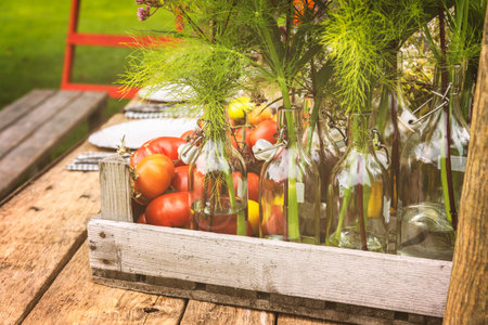 Wooden table setup for dinner with vase bottles and fresh tomatoes.