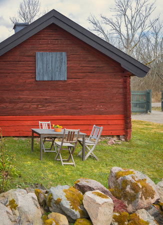 Red garden cottage with table and chairs, in rural setting.の写真素材