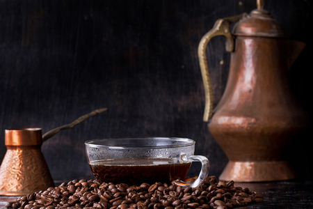 A cup of freshley made coffee on a pile of coffee beans with copper coffee maker and cezveの写真素材