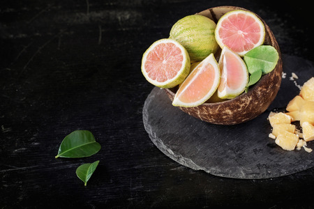 Pink tiger lemons sliced into pieces with lime leaves and lemon and lime in coconut shell with palm sugar over round slate boardの写真素材