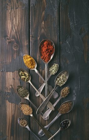 Selection of various spices and herbs in old metal spoons over a rustic wooden background. Top viewの写真素材