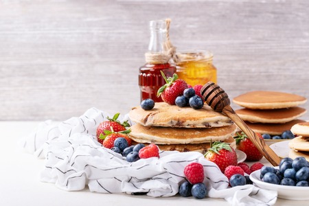 Blueberry pancakes served with strawberries, blueberries, raspberries, honey and maple syrup over white backgroundの写真素材