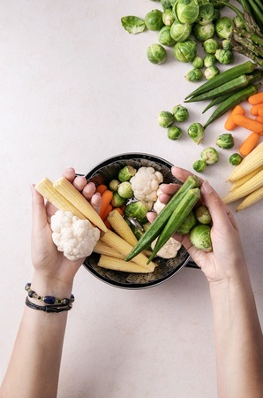 Fresh greens ready to cook: Brussels cabbage, asparagus, baby corn, cauliflower and bamia with metal steamer over a white background. Top viewの写真素材