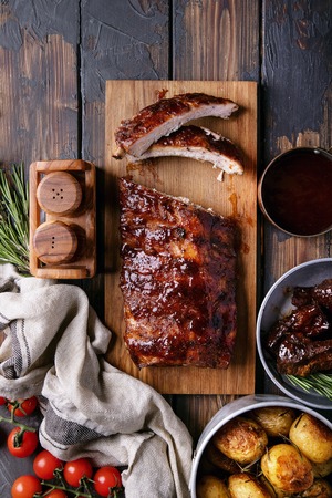 Home made pork and beef ribs, glazed with barbecue sauce served with baked rosemary potatoes, herbs and tomatoes, decorated with napkins over a rustic wooden background. Top Viewの写真素材