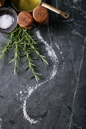 Extra Virgin Olive Oil in a copper pot with ceramic jug, rosemary and salt over a grey marble background. Top view. Copy spaceの写真素材
