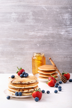 Blueberry pancakes served with strawberries and blueberries over white background. Copy spaceの写真素材