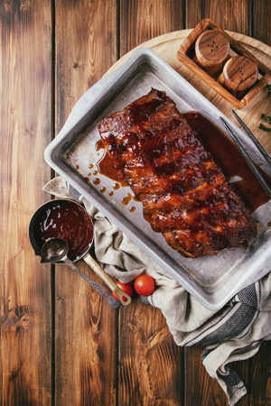 Home made pork ribs, glazed with barbecue sauce served with herbs and tomatoes, decorated with napkins over a rustic wooden background. Top View. Copy Spaceの写真素材