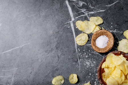 Bowl of home made potato chips served with fleur de sel salt on dark texture background. Top view,...
