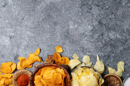 Bowl of home made potato salted and paprika chips served with mustard and fleur de sel salt on dark...