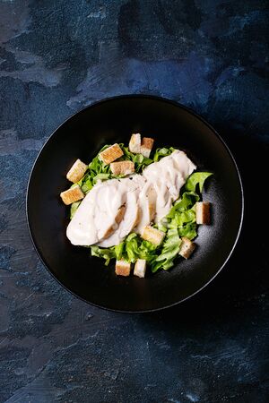 Classic caesar salad: chicken brests, lettuce, salt, cheese, sauce and black pepper over blue texture background. Top view, flat lay. Copy spaceの写真素材