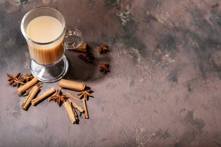 Masala chai served with cinnamon sticks and anise over dark wooden background