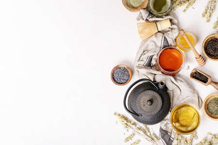 Variety of green, black and matcha tea with glass cups, wooden bowls and teapot over a white texture background. Top view. Copy Spaceの写真素材
