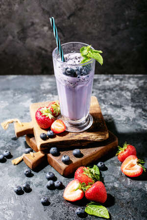 Fresh strawberry and blueberry milkshakes served with berries and mint over dark texture backgroundの写真素材
