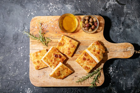 Baked focaccia bread served with olives. Traditional Italian Focaccia with rosemary over dark...