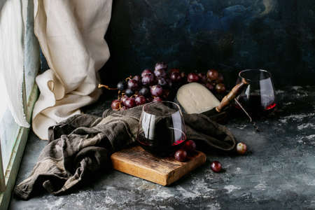 Glass of red wine served with cheese gauda and red grapes over dark texture backgroundの写真素材