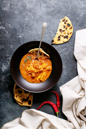 Chicken tikka masala spicy curry meat served in black ceramic plate over wooden background. Top...