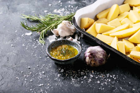 Raw potatoes with fresh rosemary and garlic over dark texture background.の写真素材