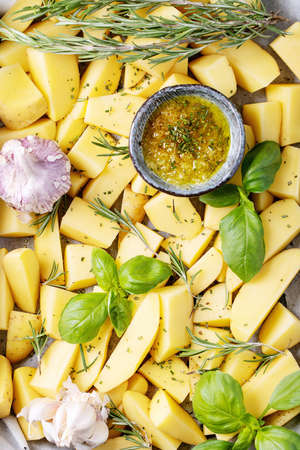 Raw potatoes with fresh rosemary, basil and garlic over dark texture background. Top view, flat lay. Copy spaceの写真素材