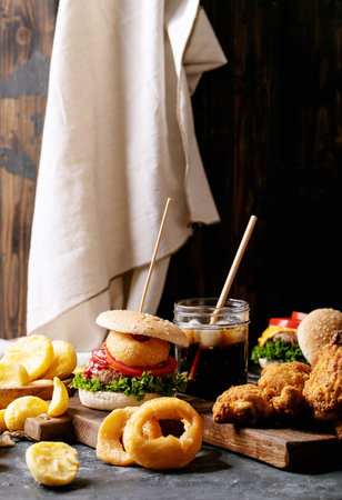 Home made burgers with onion rings and fried potatoes served with cola and crispy fried breaded chicken fillet on dark texture backgroundの写真素材