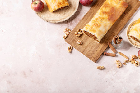 Apple strudel served with fresh apples, cinnamon sticks and walnuts over white texture backgroundの写真素材