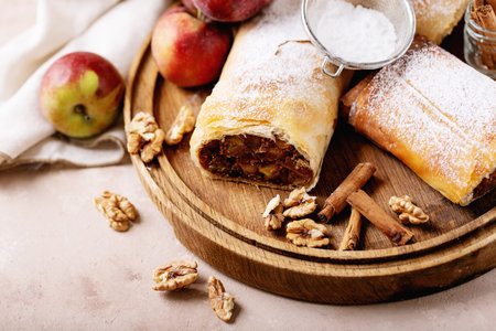Apple strudel served with fresh apples, cinnamon sticks and walnuts over white texture backgroundの写真素材