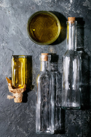 Olive oil in glass bowl with empty glass bottles over dark texture backgroundの写真素材