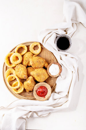 Crispy fried breaded chicken fillet with fried onion rings and potatoes served with sauce over white texture background. Top view, flat lay. Copy spaceの写真素材