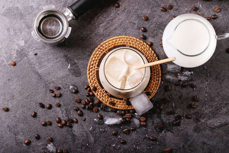 Glass of ice coffee with ice cubes served with cream and coffee beans over dark texture background. Top view, flat lay. copy spaceの写真素材