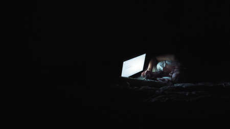Nice girl watching something on a laptop monitor. Night atmosphere in the apartment. Laptop screen illuminates the girls faceの写真素材
