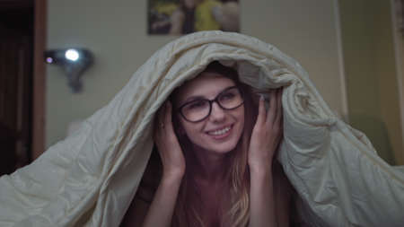 woman rejoices watching comedy at home, girl lying on the bed under the blanketの写真素材