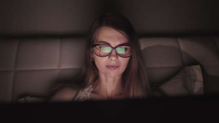 Attractive young businesswoman working at night via computer at office with, closeup of hipster student girl browsing the internet, looking at monitor of modern computer, focus on the glassesの写真素材