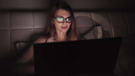 Business woman keyboarding on laptop computer doing job overworking at evening, female financial expert reading website information on netbook before deadlineの写真素材