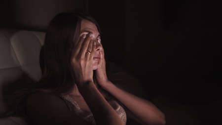 Young Girl lying on a sofa with a laptop and yawns few times. Trying to work at night. Girl with long hair and wear a white shirt. Legs are covered with a plaidの写真素材