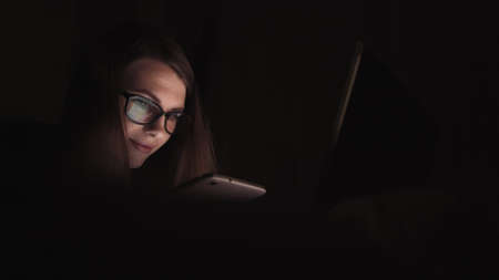 Close up of lonely young woman lying on sofa and using smartphone at night. Depressed millennial female staring at mobile phone screen and thinking. Concept of painful breakupの写真素材