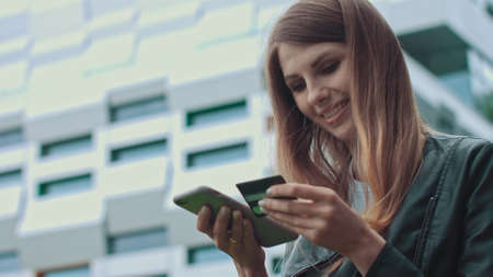 Smiling young female customer holding credit card and smartphone, on modern home background. Happy women shoppers using instant simple mobile payments while shopping online. Electronic banking serviceの写真素材