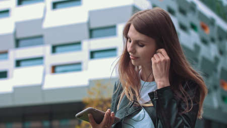Attractive girl, student, in modern clothes Uses a mobile phone to listen to good mood music, music lover puts a favorite song, happy woman uses roaming, high speed connection 5Gの写真素材