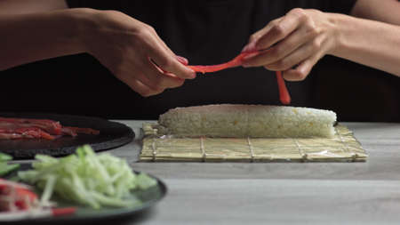 Japanese chef prepares sushi rolls with salmon and avocado. Cook hands making Japanese sushi roll on the bamboo mat. Delicious Japanese food, low-angle viewの写真素材