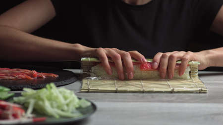 Japanese chef prepares sushi rolls with salmon and avocado. Cook hands making Japanese sushi roll on the bamboo mat. Delicious Japanese food, low-angle viewの写真素材