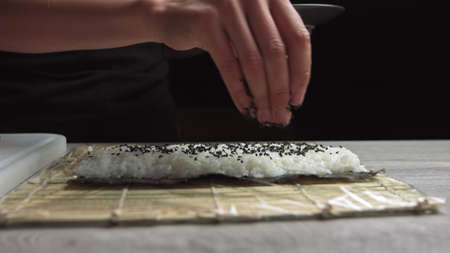 Chefs hands sprinkle sesame seeds on the inside out sushi. Japanese chef in black gloves at work preparing sushi roll with salmon and avocado.の写真素材