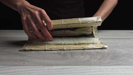 Chef in gloves is cookiing sushi maki using mat. Maki are made of rice, nori seaweed, cucumber, cream cheese. Appetizing and nutritious japanese food.の写真素材