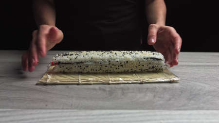 Chef in gloves is cookiing sushi maki using mat. Maki are made of rice, nori seaweed, cucumber, cream cheese. Appetizing and nutritious japanese food.の写真素材