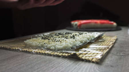 Chefs hands sprinkle sesame seeds on the inside out sushi. Japanese chef in black gloves at work preparing sushi roll with salmon and avocado.の写真素材