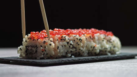 Sticks Take Sushi from Sushi box. Variety of types sushi with red caviar, fish, Philadelphia cheese and chopsticks close-up. Set of delicious Japanese sushi rolls.の写真素材